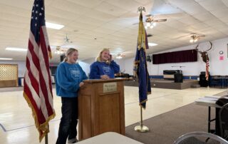 Two people speaking at a podium with flags.